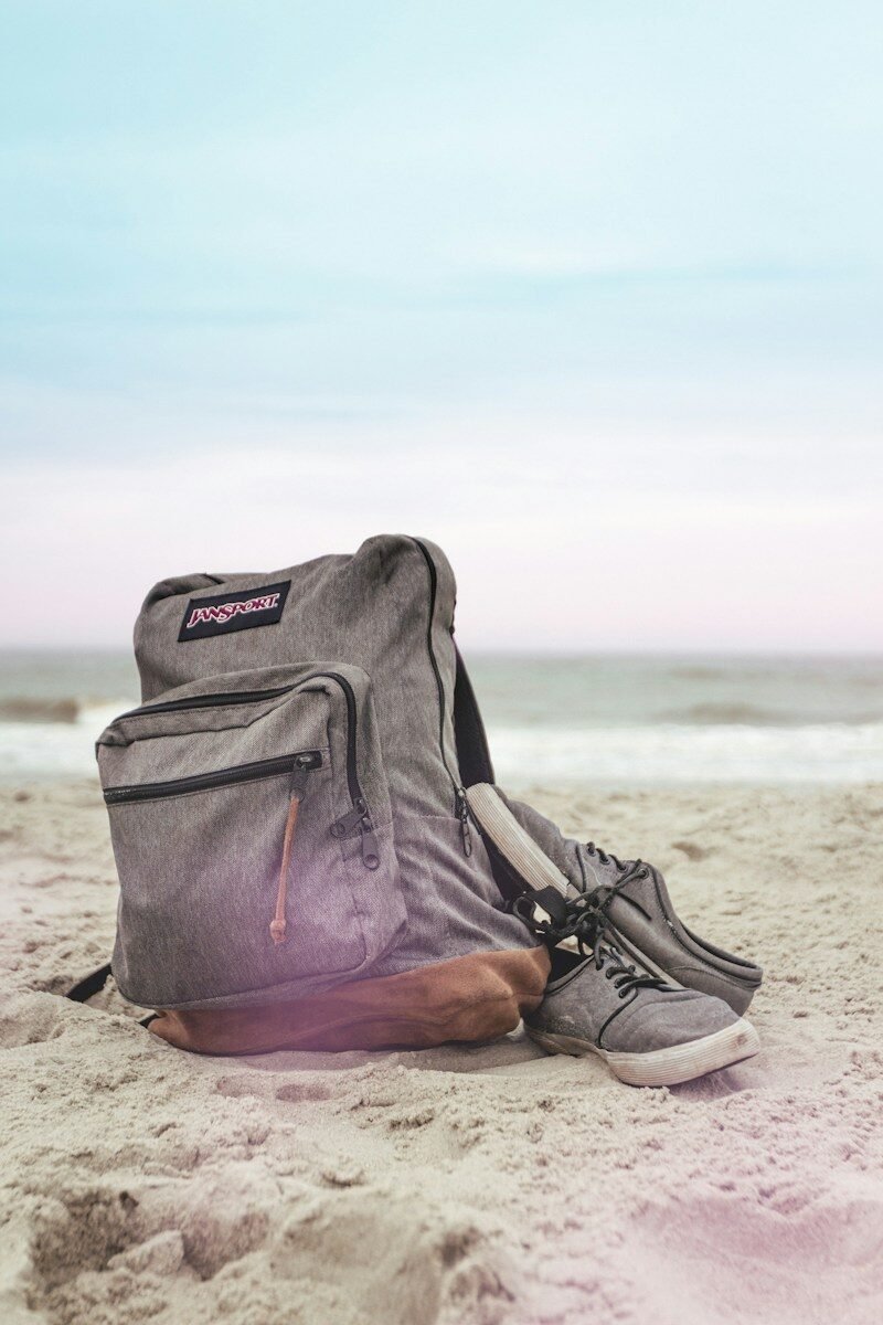 A backpack resting on sand near the water