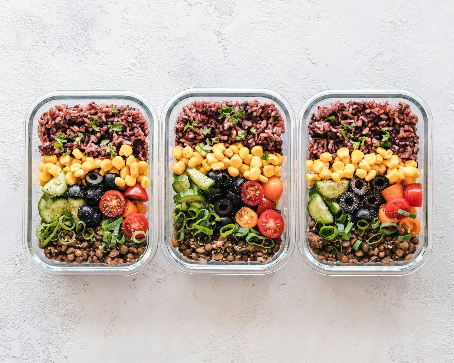Glass containers filled with rice, lentils, corn and vegetables for meal prep